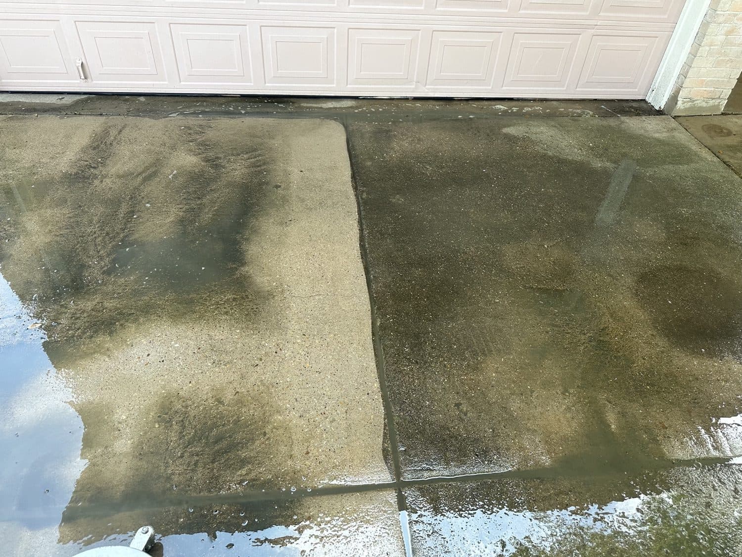 A concrete garage apron showing algae buildup beside a freshly cleaned strip in the Austin, TX area